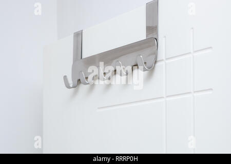 Metal hooks for towels hanging on white door in bathroom. Stock Photo