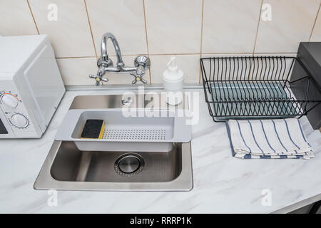 Modern kitchen sink and faucet, plastic sponge drying rack and empty dish drying rack. Stock Photo