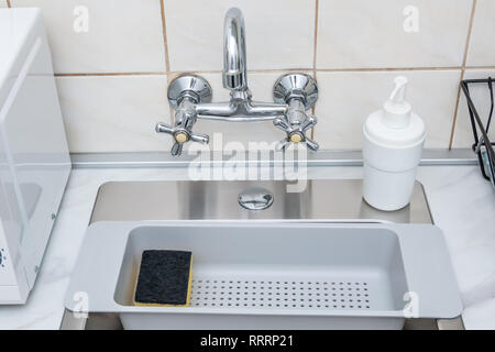 Modern kitchen sink and faucet, plastic sponge drying rack and dish washing liquid bottle. Stock Photo