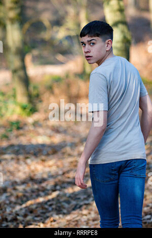 Scared or nervous teenage caucasian boy walking away through woodland on a warm spring day looking over his shoulder Stock Photo