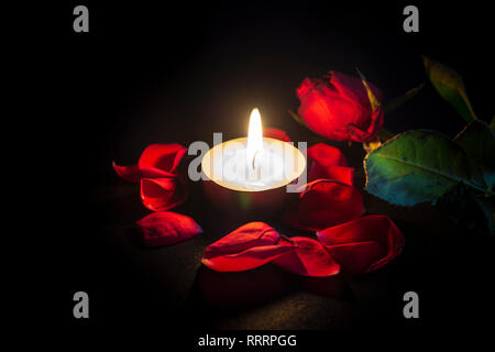 Tea candle and red rose petals with shallow depth of focus with reflection on black background Stock Photo