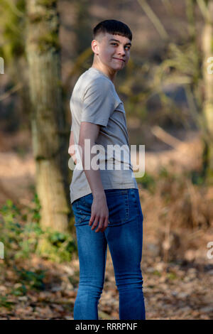 Teenage caucasian boy walking away through woodland on a warm spring day looking over his shoulder Stock Photo