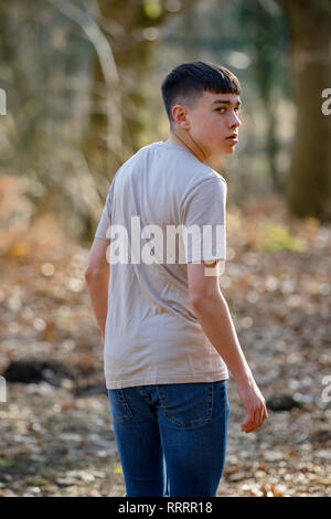 Scared or nervous teenage caucasian boy walking away through woodland on a warm spring day looking over his shoulder Stock Photo