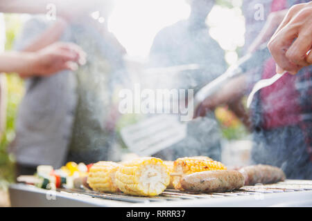 Corncobs, sausages and vegetable skewers cooking on barbecue grill