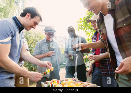 Male friends standing around barbecue grill in backyard Stock Photo