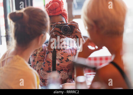 Young woman photographing friends with camera in restaurant Stock Photo
