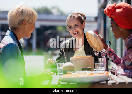 Young women friends eating dim sum lunch at sunny sidewalk cafe Stock Photo
