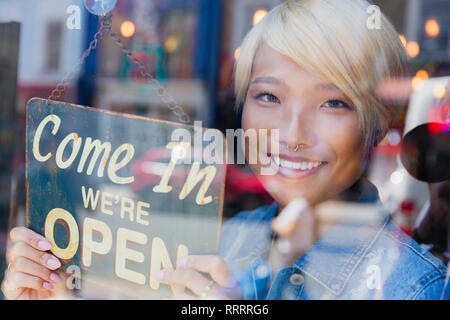 Portrait confident young female shop owner holding Open sign at window Stock Photo