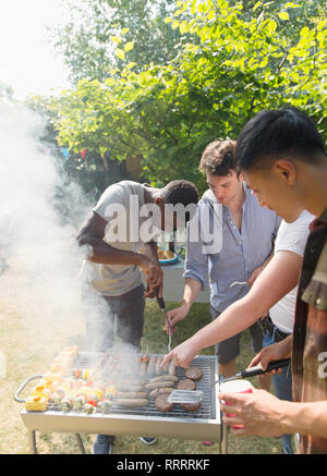 Male friends at barbecue grill in sunny backyard Stock Photo