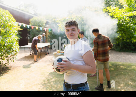 Portrait confident teenage boy with soccer ball, enjoying backyard barbecue Stock Photo