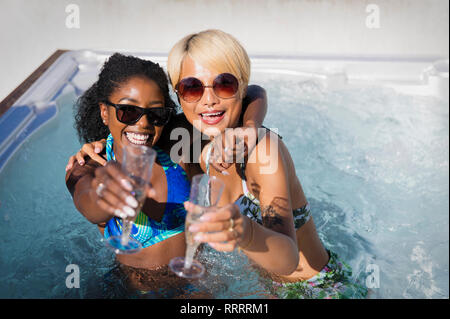Portrait exuberant young women friends drinking champagne in sunny hot tub Stock Photo
