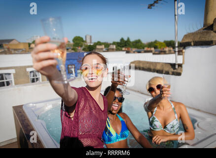 Portrait confident, carefree young women friends drinking champagne in sunny rooftop hot tub Stock Photo