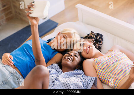 Young women friends using instant camera on bed Stock Photo