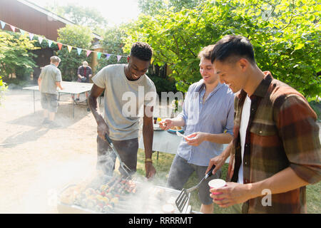 Young men barbecuing in sunny backyard Stock Photo