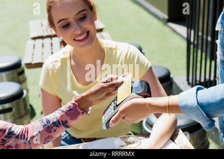 Young woman waitress with smart card at sunny sidewalk cafe Stock Photo