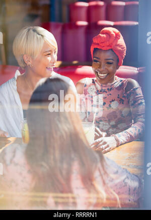 Happy young women friends drinking in sunny restaurant Stock Photo