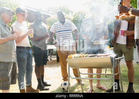 Male friends drinking beer and barbecuing in sunny summer backyard Stock Photo