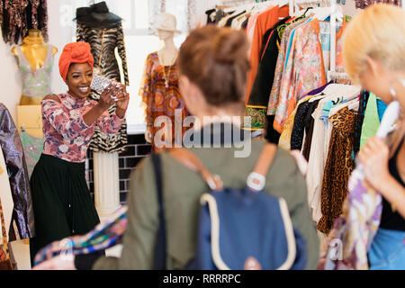 Young woman with camera phone photographing friends shopping in clothing store Stock Photo