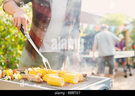 Man barbecuing corn, sausage and vegetable kebabs Stock Photo