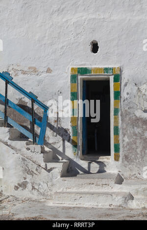 White weathered wall of a house with opened door, framed with yellow and green color. Staris on the left with a blue handrail. Sidi Kaouki, Morocco. Stock Photo