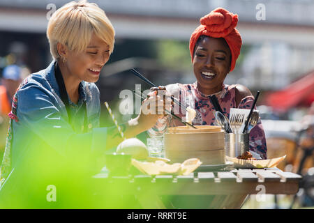 Young women friends enjoying dim sum lunch with chopsticks at sunny sidewalk cafe Stock Photo