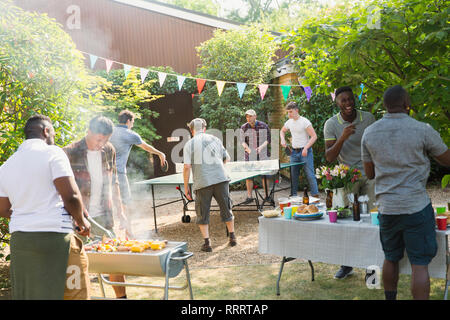 Male friends playing ping pong, enjoying backyard barbecue Stock Photo
