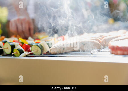 Close up sausages and vegetable skewers cooking, steaming on barbecue grill