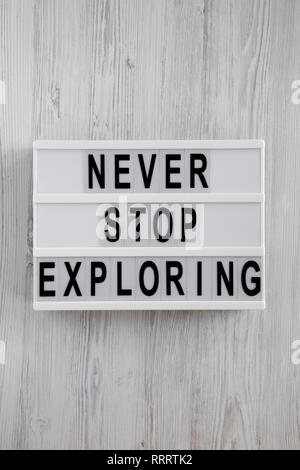 Lightbox with text 'Never stop exploring' over white wooden surface, top view. Overhead, flat lay, from above. Stock Photo