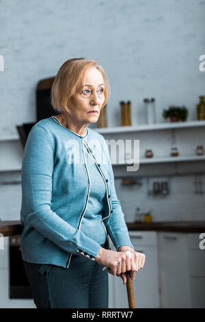 depressed senior woman holding walking stick and looking away at home Stock Photo