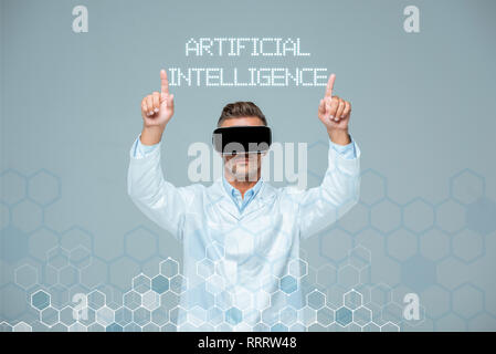 scientist in virtual reality headset touching artificial intelligence lettering with two fingers isolated on grey Stock Photo