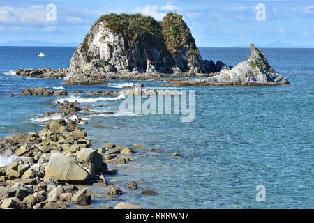 Horizontal view of rocks stretching from shore to rocky islet near harbor mouth in Mangawhai Heads. Stock Photo