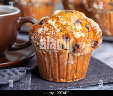 Closeup of a chocolate chip muffin with a cup of coffee and muffins in background Stock Photo