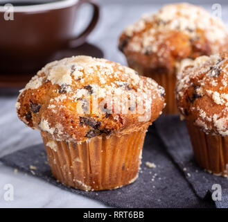 Closeup of a chocolate chip muffin with a cup of coffee and muffins in background Stock Photo