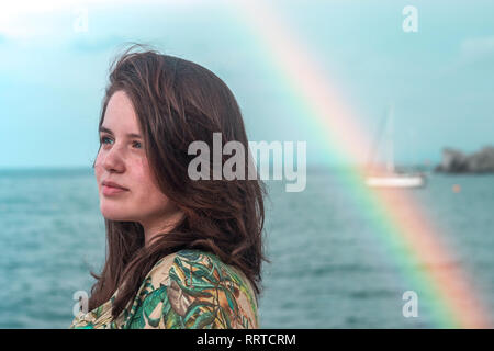 Portrait of a young normal red hair woman smiling with rainbow and sea in the background. Copy space Stock Photo