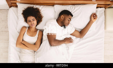 Sad woman lying in bed with sleeping man Stock Photo