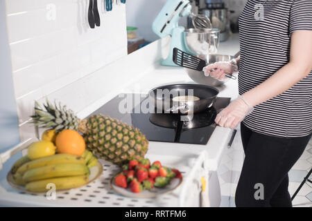 Young woman making pancakes on the kitchen. Fresh fruits on the table Stock Photo