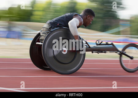 Determined young male paraplegic athlete speeding along sports track in wheelchair race Stock Photo