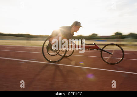 Determined teenage boy paraplegic athlete speeding along sports track in wheelchair race Stock Photo