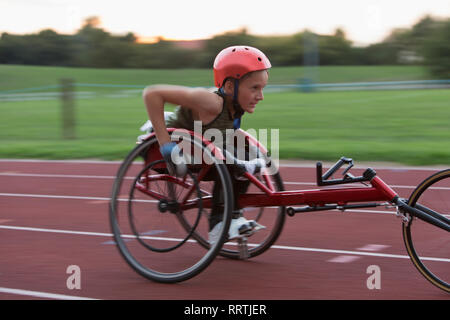 Determined teenage girl paraplegic athlete speeding along sports track in wheelchair race Stock Photo