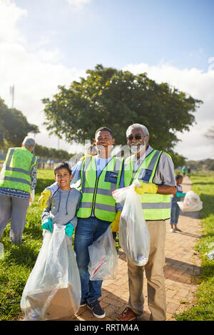 Portrait happy multi-generation men volunteering, cleaning up litter in sunny park Stock Photo