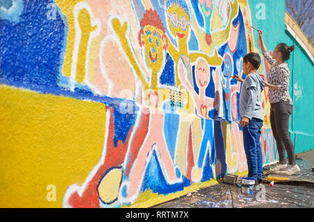 Mother and son volunteers painting vibrant mural on sunny wall Stock Photo