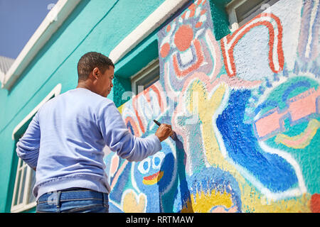 Male volunteer painting vibrant mural on sunny wall Stock Photo