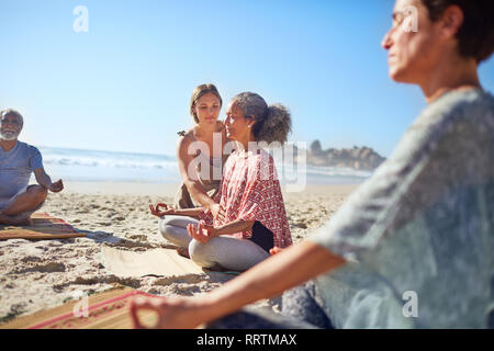Serene women meditating on sunny beach during yoga retreat Stock Photo