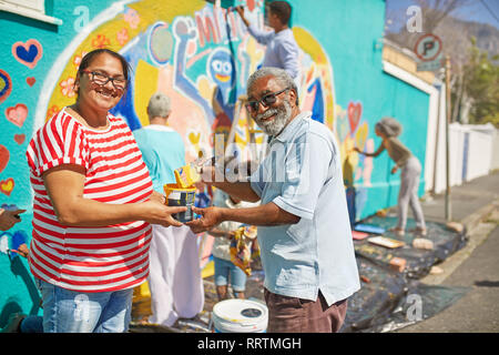 Portrait happy community volunteers painting mural on sunny urban wall Stock Photo