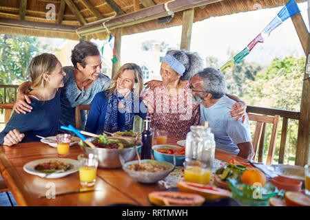 Happy friends hugging, enjoying healthy meal in hut during yoga retreat Stock Photo