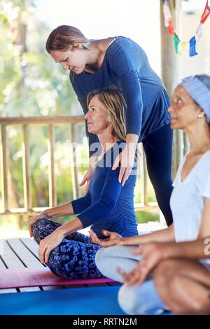 Female instructor adjusting student’s shoulders during yoga retreat Stock Photo