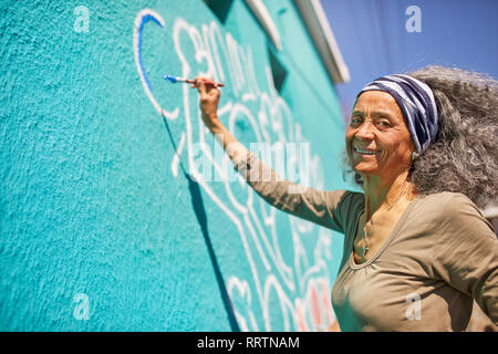 Portrait happy senior female volunteer painting on sunny wall Stock Photo