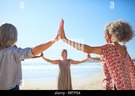 Women joining hands in circle on sunny beach during yoga retreat Stock Photo