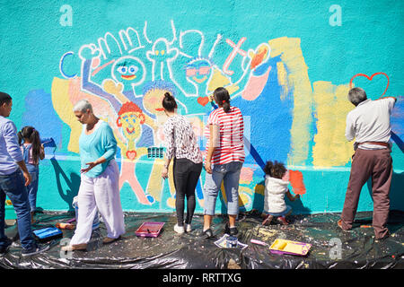 Community volunteers painting vibrant mural on sunny wall Stock Photo