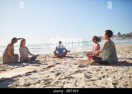 Group meditating on sunny beach during yoga retreat Stock Photo